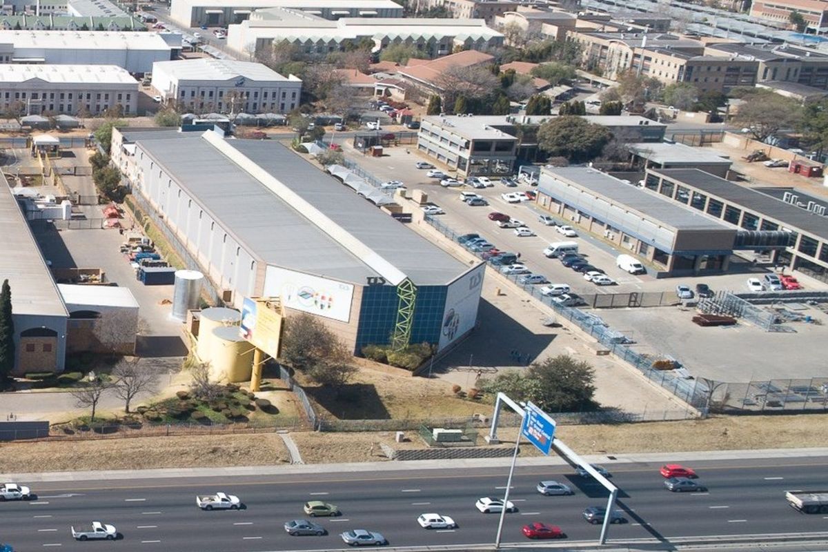 Aerial view of an industrial warehouse facility featuring extensive parking, secure perimeter fencing, and direct proximity to a major highway.