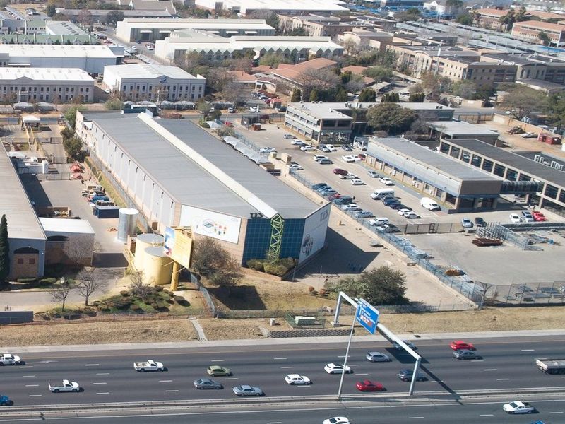 Aerial view of an industrial warehouse facility featuring extensive parking, secure perimeter fencing, and direct proximity to a major highway.