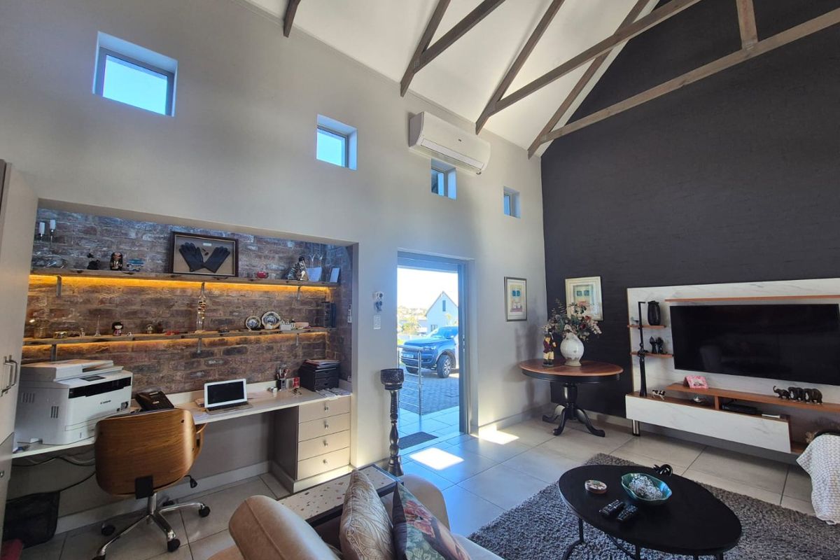 Spacious living area featuring a vaulted ceiling with exposed timber trusses, an integrated brick-walled study nook, and modern tiled flooring.