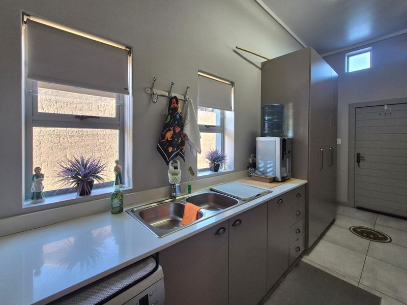 A functional scullery featuring a double bowl stainless steel sink, stone countertops, ample built-in cabinetry, and tiled flooring.
