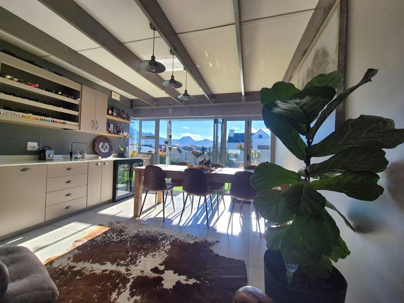 Open-plan living and dining area featuring exposed ceiling beams, modern built-in cabinetry with wine storage, and bi-fold doors opening to a scenic view.