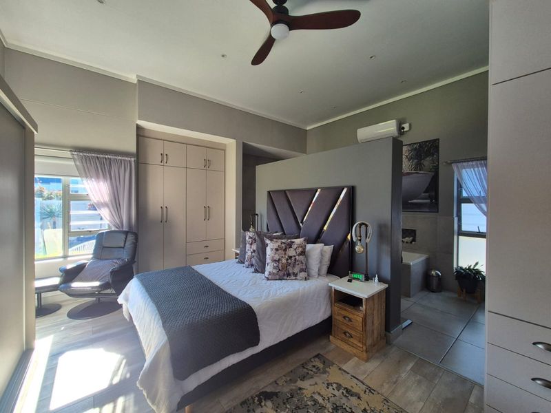 Spacious bedroom featuring built-in cupboards, a ceiling fan, air conditioning, and an open-plan en-suite bathroom area with modern finishes.