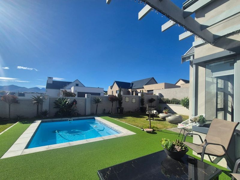 A well-maintained outdoor pool area featuring a swimming pool, artificial lawn, and a pergola, set within a secure walled garden.