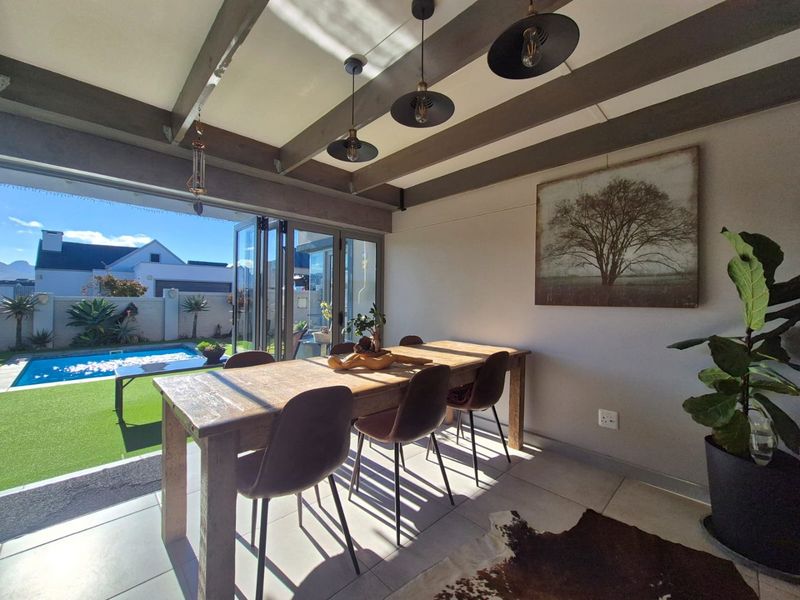 Covered patio area featuring exposed timber beams, tiled flooring, and bi-fold doors opening directly onto a private garden and swimming pool.