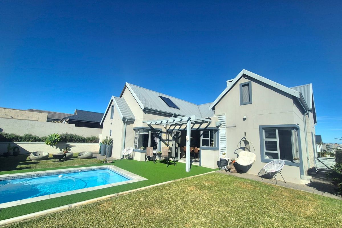 Rear exterior view featuring a swimming pool, artificial lawn, and a covered pergola attached to the main house structure.