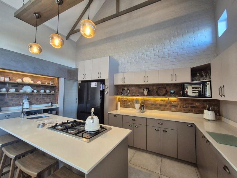 Modern kitchen featuring exposed brick walls, vaulted ceilings with timber beams, a central island with gas cooktop, and high-quality cabinetry with integrated lighting.