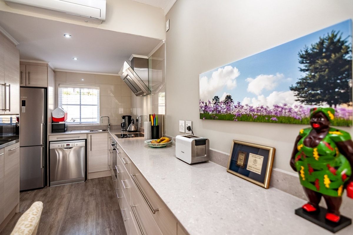 Modern kitchen featuring light wood-tone cabinetry, stone countertops, stainless steel appliances, and a sleek extractor fan, complemented by recessed lighting and air conditioning.