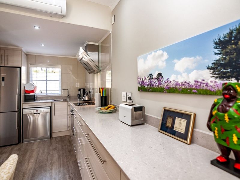 Modern kitchen featuring light wood-tone cabinetry, stone countertops, stainless steel appliances, and a sleek extractor fan, complemented by recessed lighting and air conditioning.