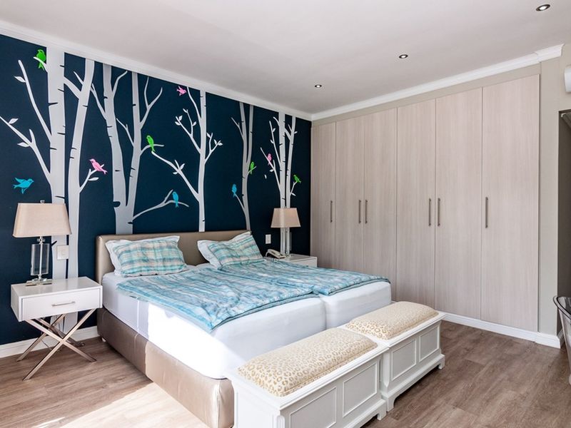 A well-maintained bedroom featuring extensive built-in cupboards, modern laminate flooring, recessed lighting, and a wall-mounted air conditioning unit.
