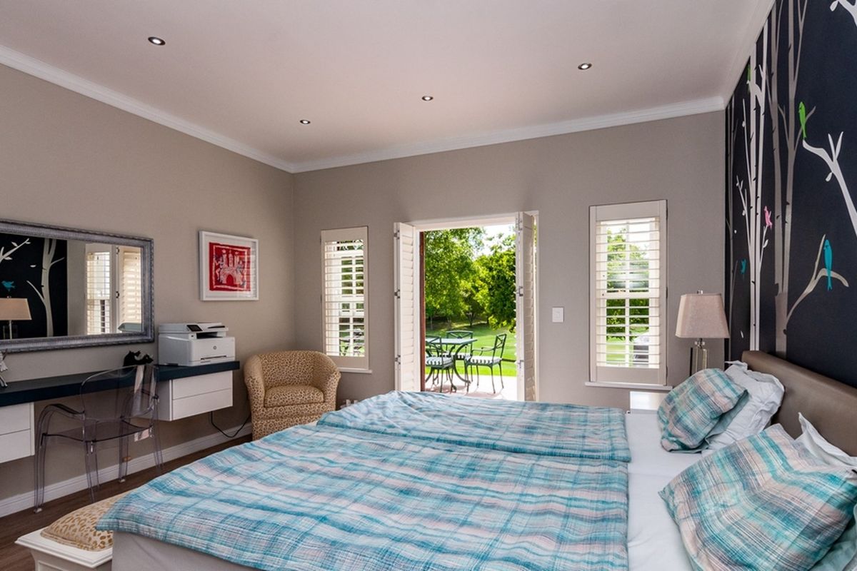 Spacious bedroom featuring recessed downlights, plantation shutters, and direct access to the garden through French doors, complemented by a built-in desk area.