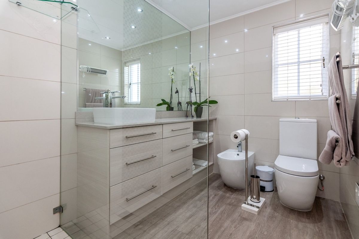 Modern bathroom featuring a sleek vanity with vessel sink, large wall mirror, bidet, toilet, and a glass-enclosed shower area with neutral tiling.