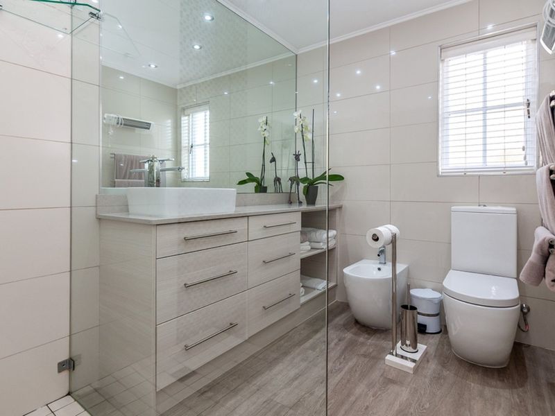 Modern bathroom featuring a sleek vanity with vessel sink, large wall mirror, bidet, toilet, and a glass-enclosed shower area with neutral tiling.