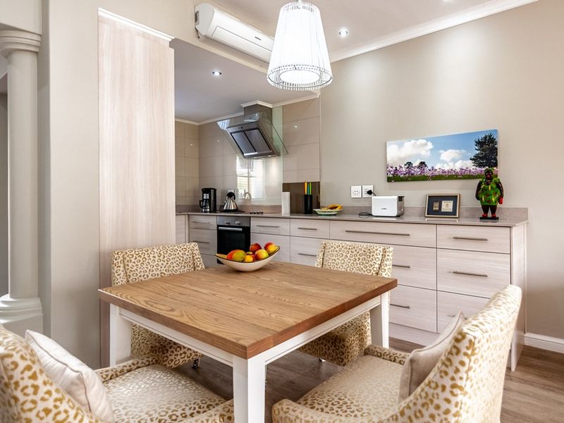 An open-plan kitchen and dining area featuring modern light-wood cabinetry, stone countertops, integrated appliances, and a split-system air conditioner.