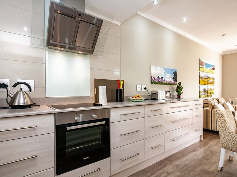 Modern open-plan kitchen featuring light wood-grain cabinetry, stone countertops, integrated stainless steel appliances, and recessed lighting, seamlessly flowing into the adjacent living area.