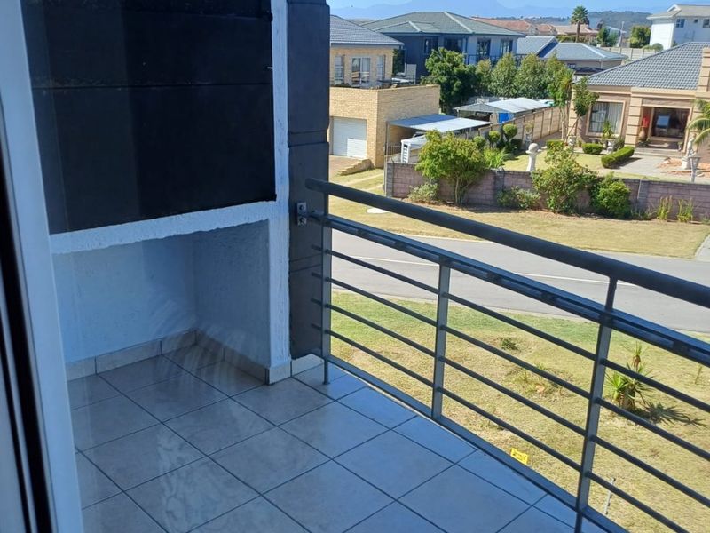 A private balcony featuring tiled flooring, a built-in braai, and a metal balustrade, offering pleasant views of the surrounding residential neighborhood.