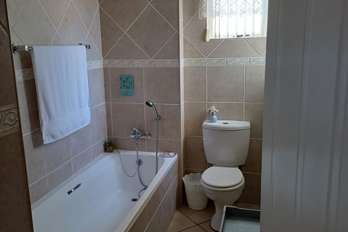 A functional bathroom featuring a built-in bathtub with shower mixer, ceramic wall and floor tiling, and a standard toilet.