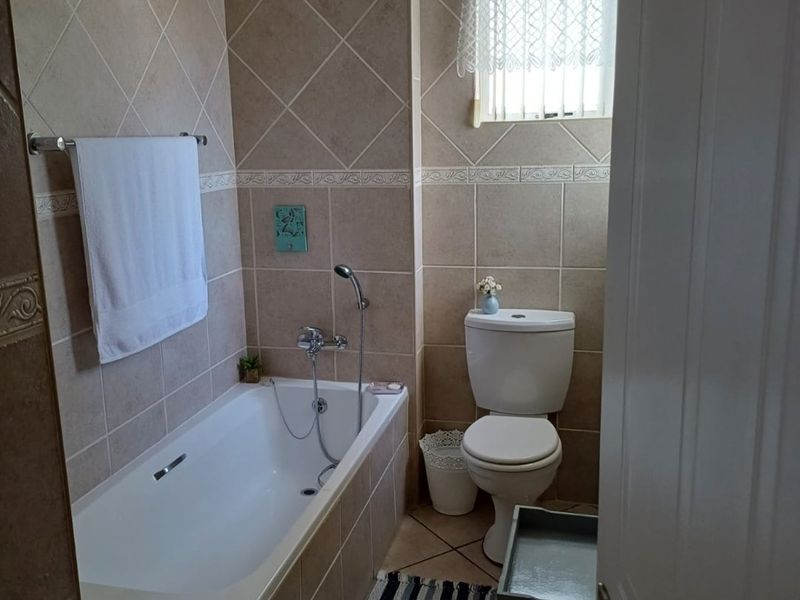 A functional bathroom featuring a built-in bathtub with shower mixer, ceramic wall and floor tiling, and a standard toilet.