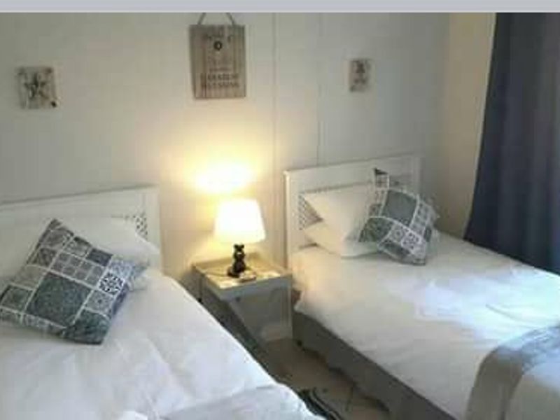 A bedroom featuring two single beds with a shared bedside table and window with curtains.