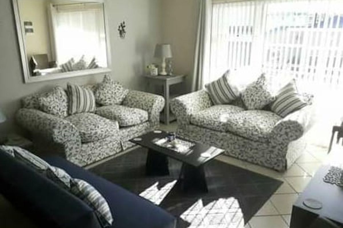 A comfortable living room featuring tiled flooring and large sliding glass doors with vertical blinds, providing natural light and access to the exterior.