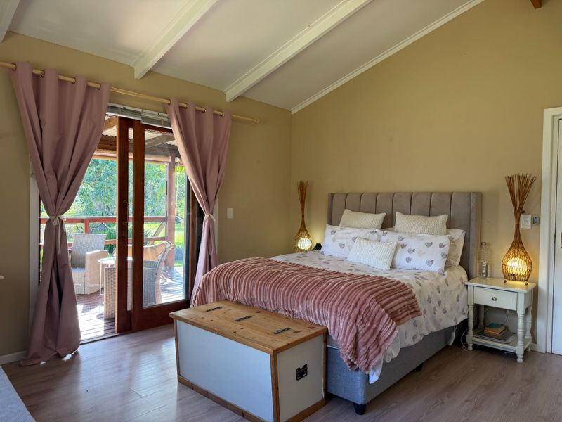 Spacious bedroom featuring vaulted ceilings with exposed beams, laminate flooring, and sliding glass doors providing direct access to an outdoor deck area.