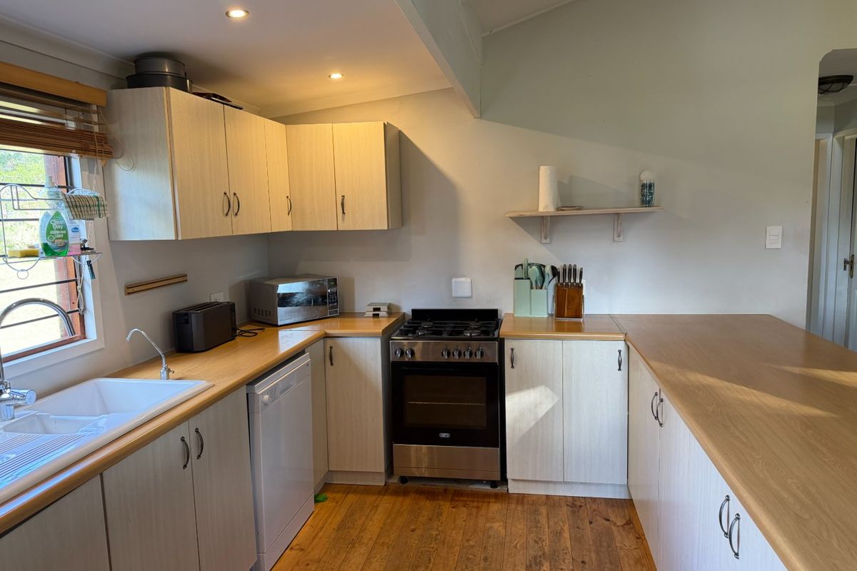 A functional kitchen featuring light wood-finish cabinetry, laminate countertops, a gas stove with oven, and timber flooring, offering a clean and practical workspace.