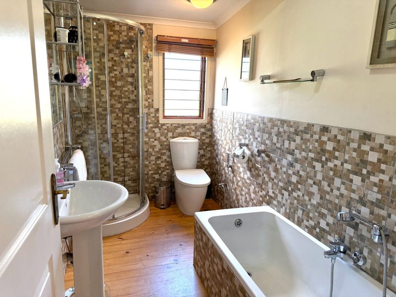 A functional bathroom featuring a corner shower, bathtub, pedestal basin, and toilet, finished with mosaic wall tiles and timber flooring.