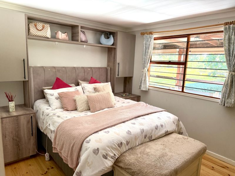 A well-maintained bedroom featuring custom built-in cabinetry surrounding the bed area, timber flooring, and louvre windows overlooking the farm grounds.