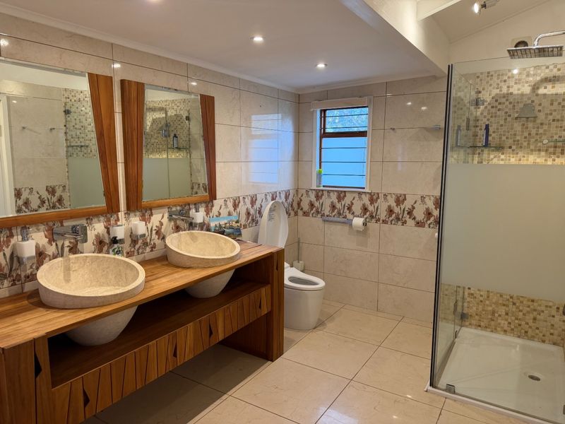 Modern bathroom featuring a double vanity with stone vessel sinks, a spacious walk-in shower with a rain shower head, and neutral tiled finishes.