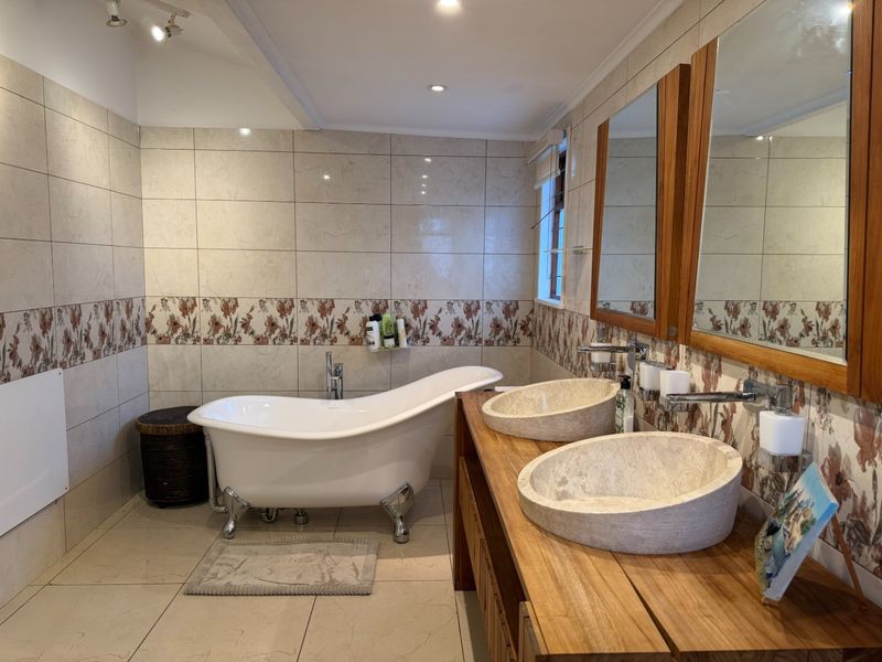 A well-appointed bathroom featuring a classic clawfoot bathtub, a wooden double vanity with stone vessel sinks, and decorative tiled wall accents.