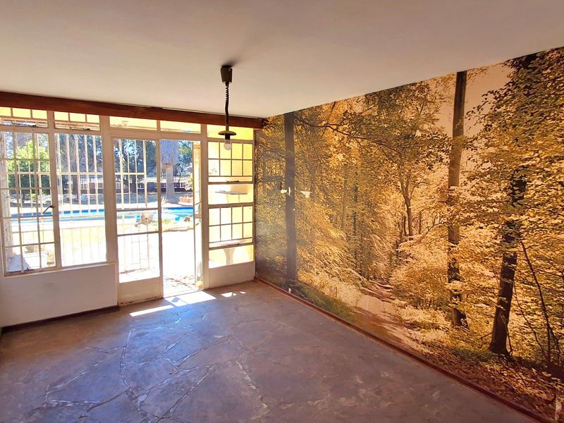 An empty living room featuring stone flooring, large windows with garden views, and a decorative forest-themed wall mural.