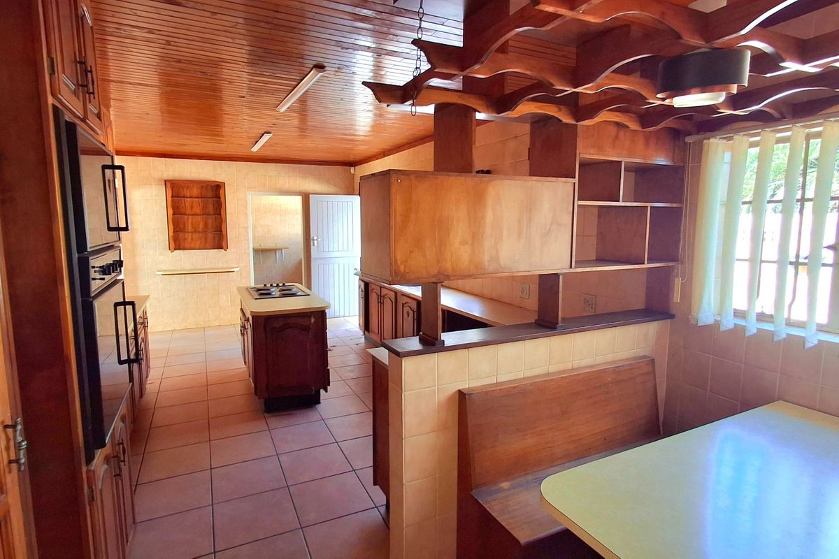 Spacious kitchen featuring extensive wooden cabinetry, a central island with hob, built-in breakfast nook, and tiled flooring throughout.