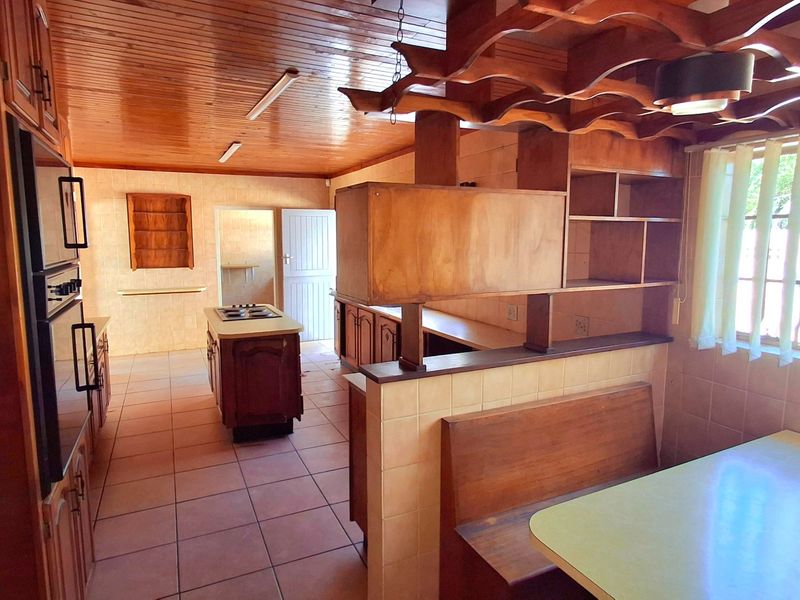 Spacious kitchen featuring extensive wooden cabinetry, a central island with hob, built-in breakfast nook, and tiled flooring throughout.
