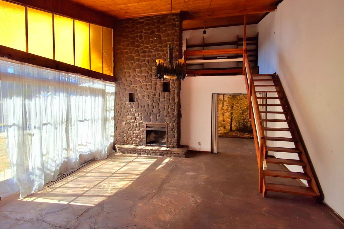 Spacious living room featuring a prominent stone fireplace, exposed timber ceiling, flagstone flooring, and a timber staircase leading to a mezzanine level.