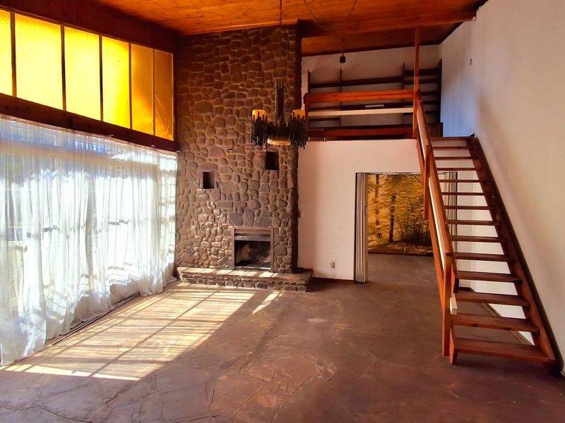 Spacious living room featuring a prominent stone fireplace, exposed timber ceiling, flagstone flooring, and a timber staircase leading to a mezzanine level.