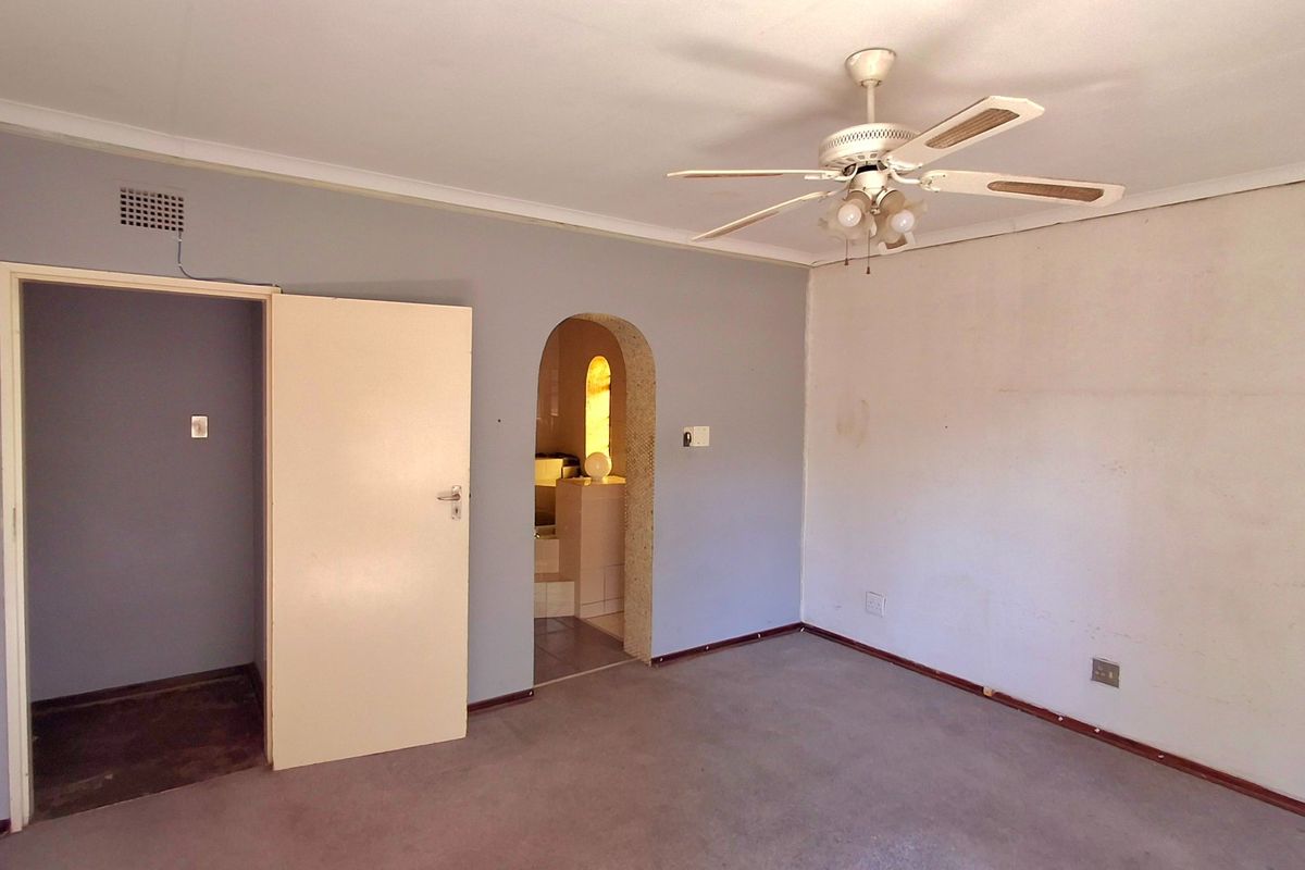 An empty bedroom featuring a ceiling fan, carpeted flooring, and an arched doorway leading to an adjacent space.