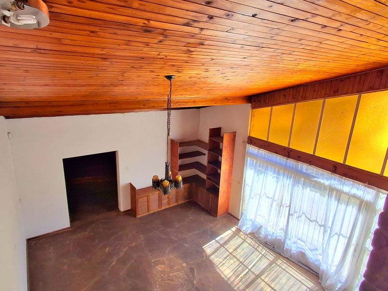 Spacious living area featuring a high timber-clad vaulted ceiling, built-in wooden shelving, and a prominent stone fireplace with large windows.
