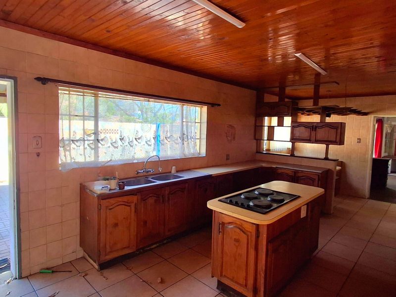 Spacious kitchen featuring wooden cabinetry, a central island with a built-in hob, double sink, and a traditional wooden tongue and groove ceiling.