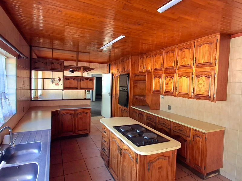 Spacious kitchen featuring extensive wooden cabinetry, a central island with a built-in hob, double sink, and a distinctive wooden ceiling.