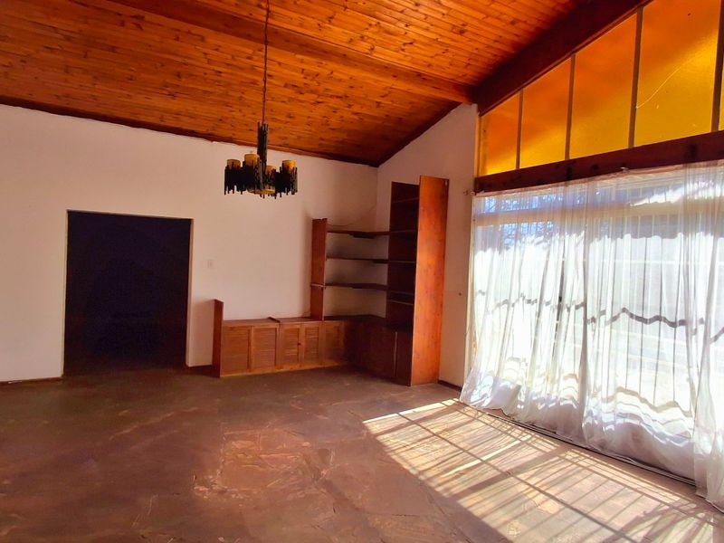 Spacious living area featuring a vaulted timber ceiling, stone flooring, built-in wooden cabinetry, and large sliding doors providing ample natural light.