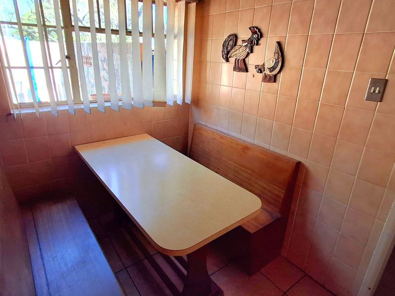 A compact kitchen breakfast nook featuring dated wall tiles, tiled flooring, and vertical blinds, offering a functional space for casual dining.