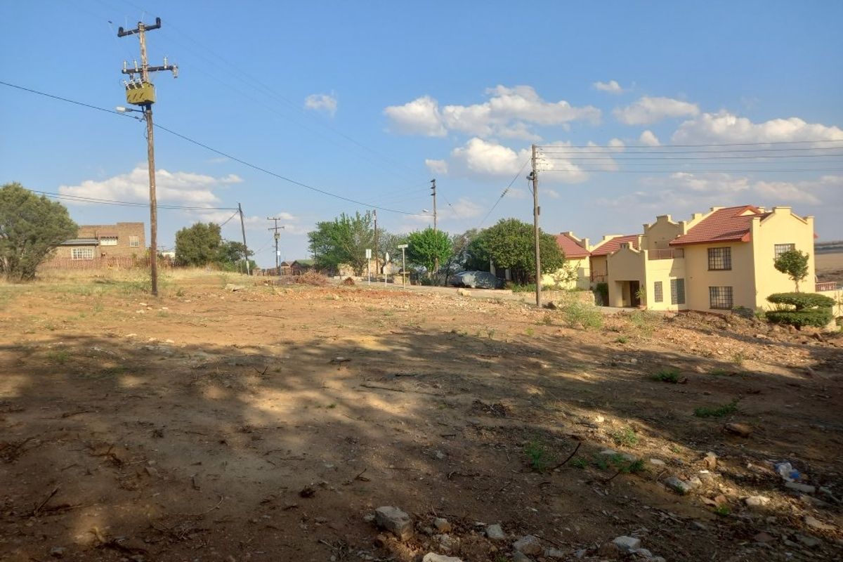 A vacant residential plot of land featuring natural terrain, utility infrastructure, and surrounding residential properties in a suburban setting.