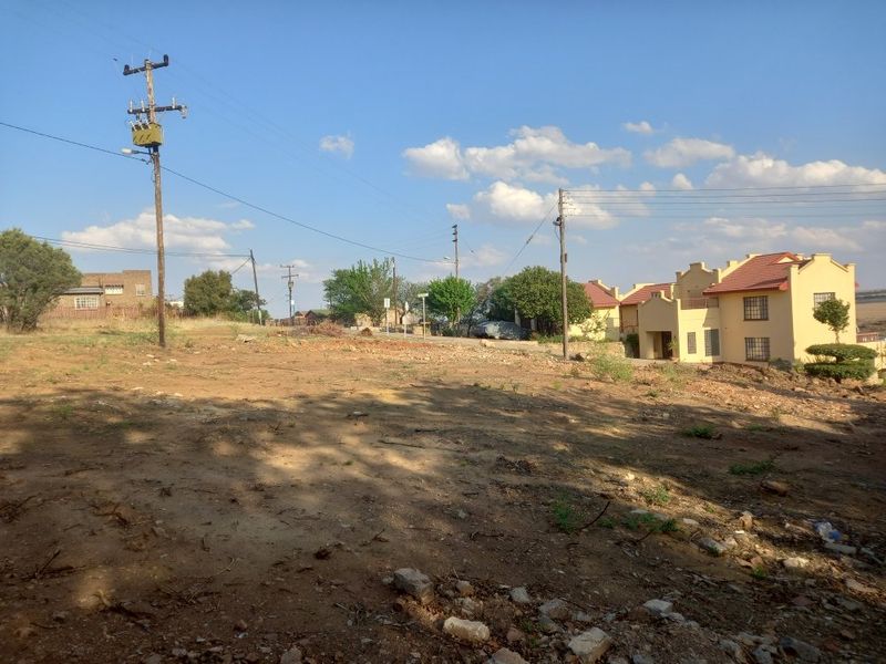 A vacant residential plot of land featuring natural terrain, utility infrastructure, and surrounding residential properties in a suburban setting.