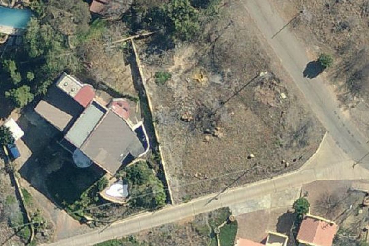 Aerial view of a vacant residential plot situated in a developed neighborhood, showing access roads and surrounding property boundaries.