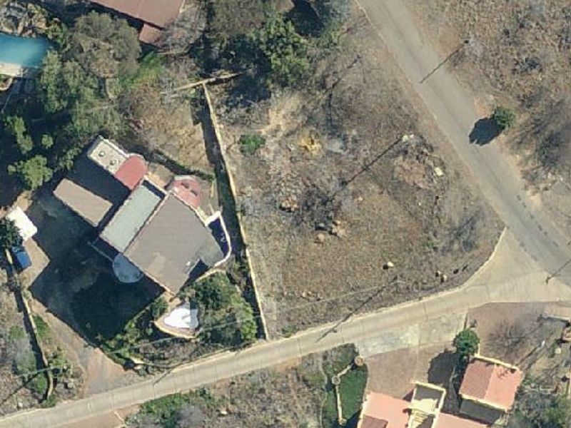 Aerial view of a vacant residential plot situated in a developed neighborhood, showing access roads and surrounding property boundaries.