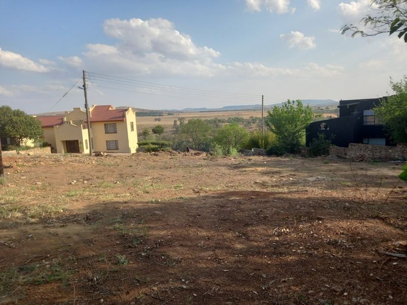A vacant residential plot of land featuring natural terrain, utility connections, and surrounding neighborhood views.
