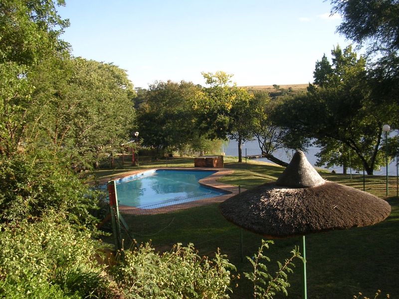 Outdoor pool area featuring a swimming pool with brick coping, set within a landscaped garden overlooking a lake.