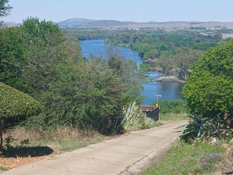 A scenic view overlooking a river with a concrete driveway leading towards the water, surrounded by established trees and natural landscape.