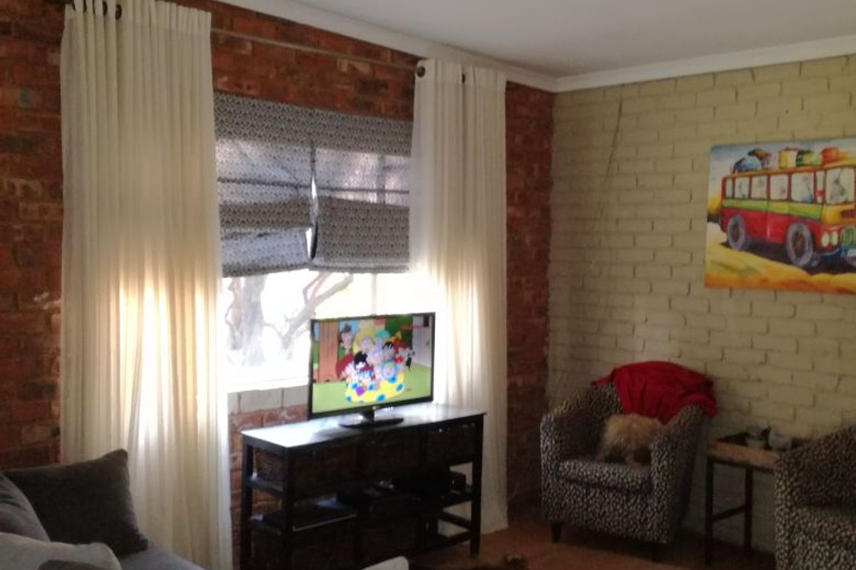 A living room featuring exposed brick and painted brick walls, tiled flooring, and an exposed timber ceiling beam.
