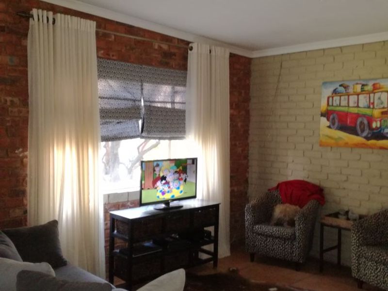 A living room featuring exposed brick and painted brick walls, tiled flooring, and an exposed timber ceiling beam.