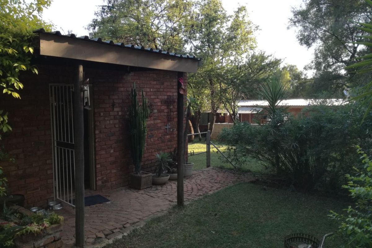 A rear view of the property featuring an exposed brick exterior, a covered patio area with brick paving, and a surrounding garden space.